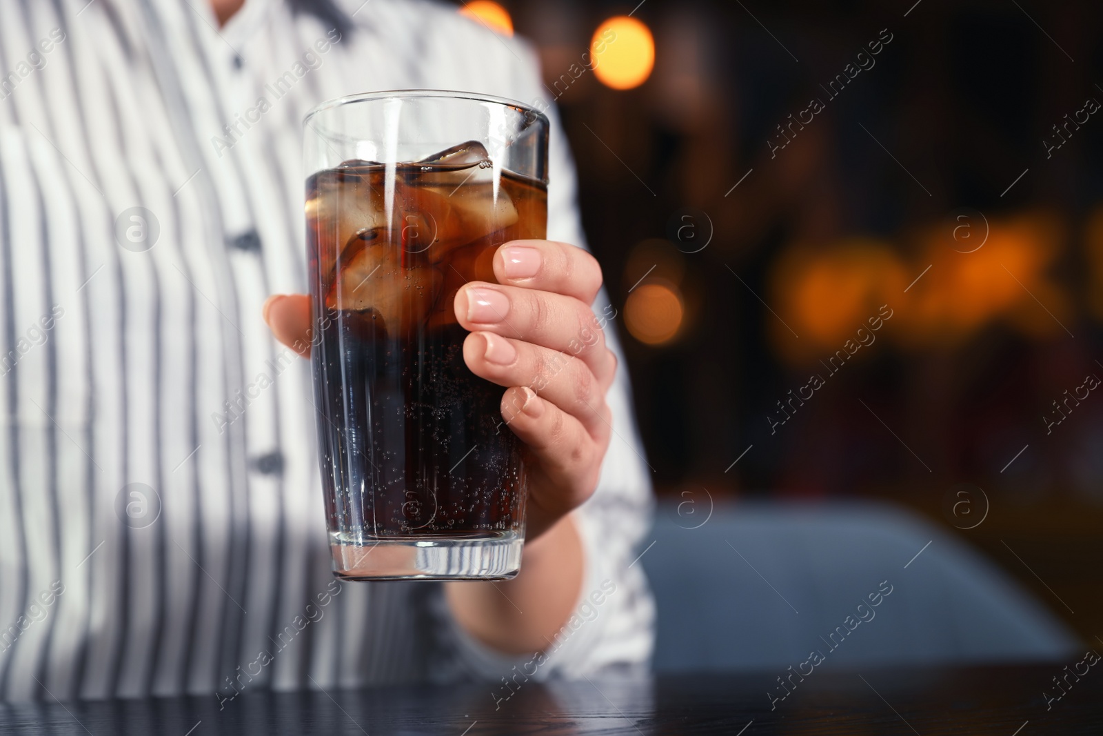 Photo of Woman with glass of refreshing cola at table indoors, closeup. Space for text