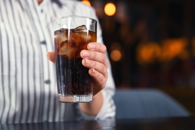 Woman with glass of refreshing cola at table indoors, closeup. Space for text