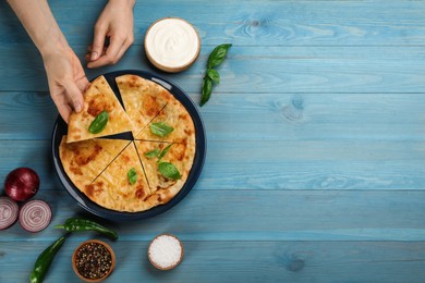 Top view of woman taking delicious khachapuri piece with cheese and basil at light blue wooden table. Space for text