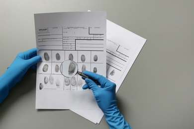 Criminologist exploring fingerprints with magnifier on grey background