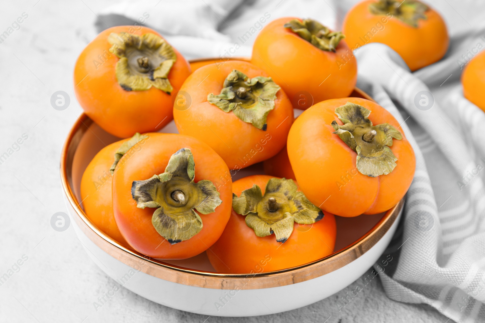 Photo of Bowl with delicious ripe juicy persimmons on white textured table