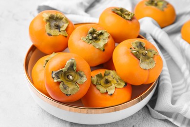 Bowl with delicious ripe juicy persimmons on white textured table