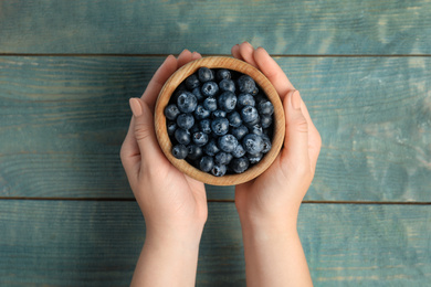 Woman holding juicy fresh blueberries at blue wooden table, top view