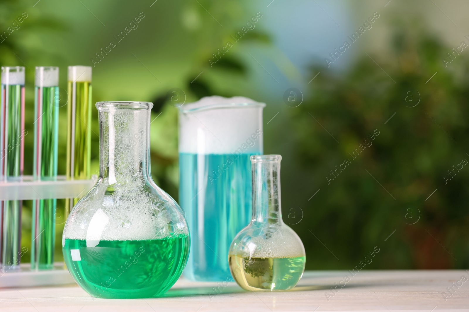 Photo of Laboratory glassware and test tubes with colorful liquids on white table outdoors, space for text. Chemical reaction