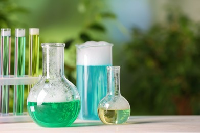 Laboratory glassware and test tubes with colorful liquids on white table outdoors, space for text. Chemical reaction