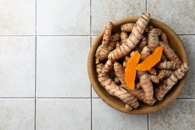 Photo of Bowl with raw turmeric roots on white tiled table, top view. Space for text