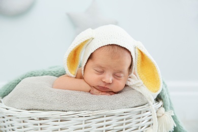 Photo of Adorable newborn child wearing bunny ears hat in baby nest indoors