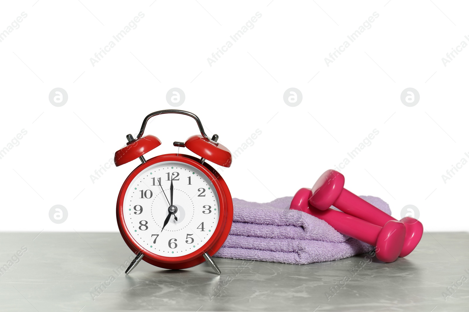 Photo of Alarm clock, towels and dumbbells on marble table against grey background. Morning exercise