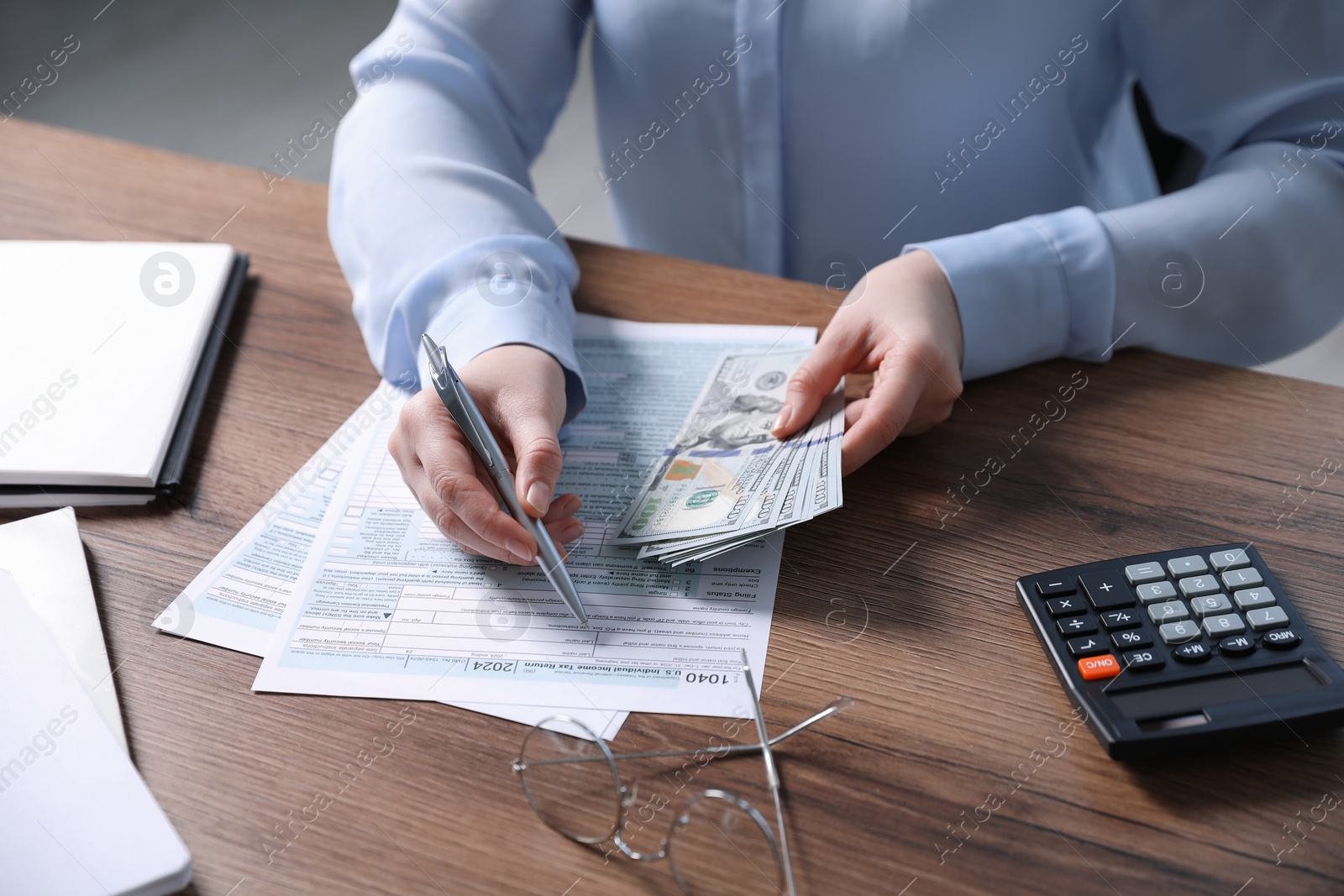 Photo of Payroll. Woman with dollar banknotes working with tax return forms at wooden table, closeup