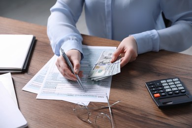 Payroll. Woman with dollar banknotes working with tax return forms at wooden table, closeup