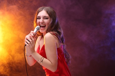 Emotional woman with microphone singing in color lights. Space for text