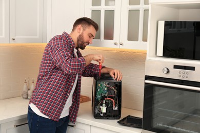 Man with screwdriver fixing coffee machine at table in kitchen