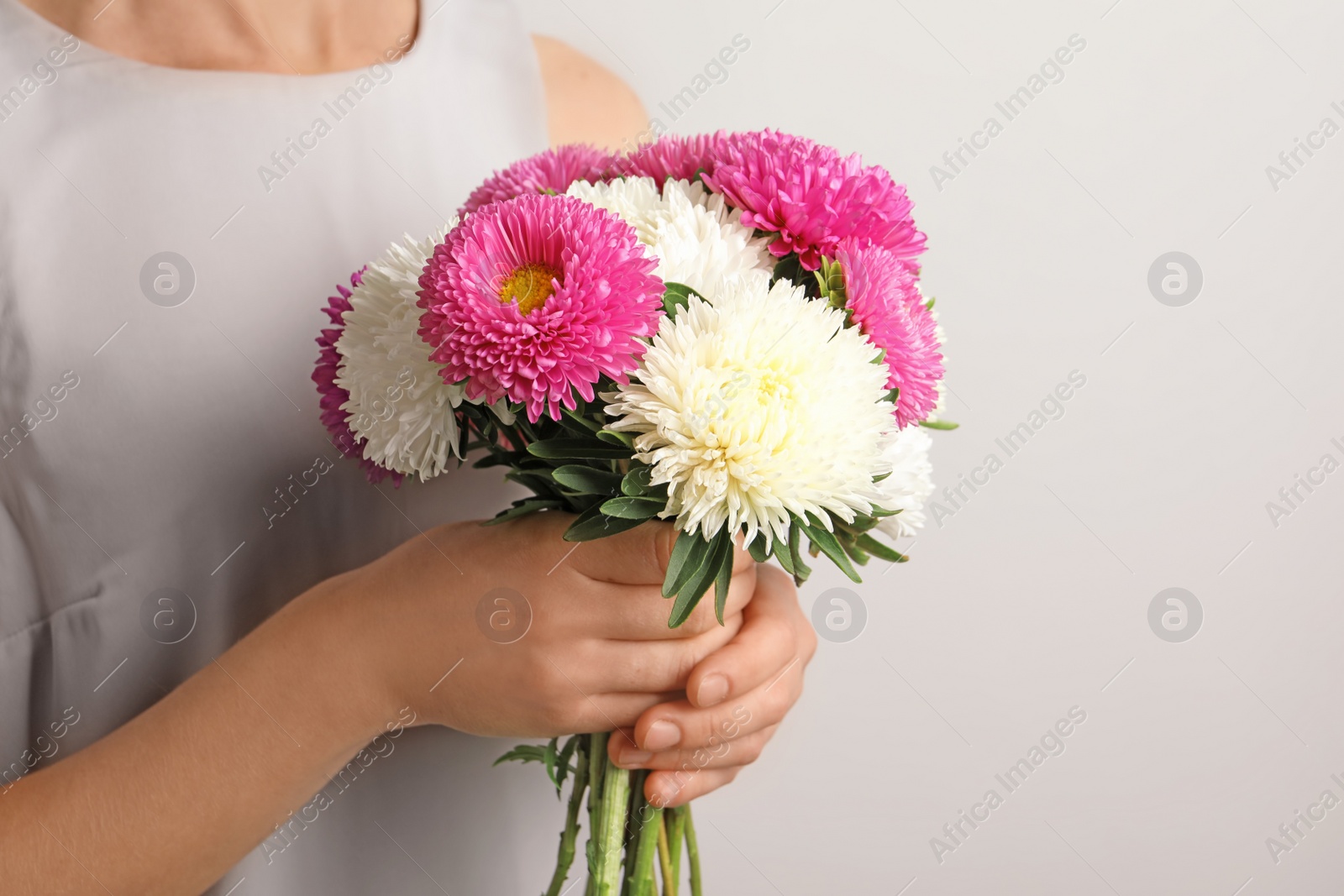 Photo of Woman holding beautiful aster flower bouquet against light background