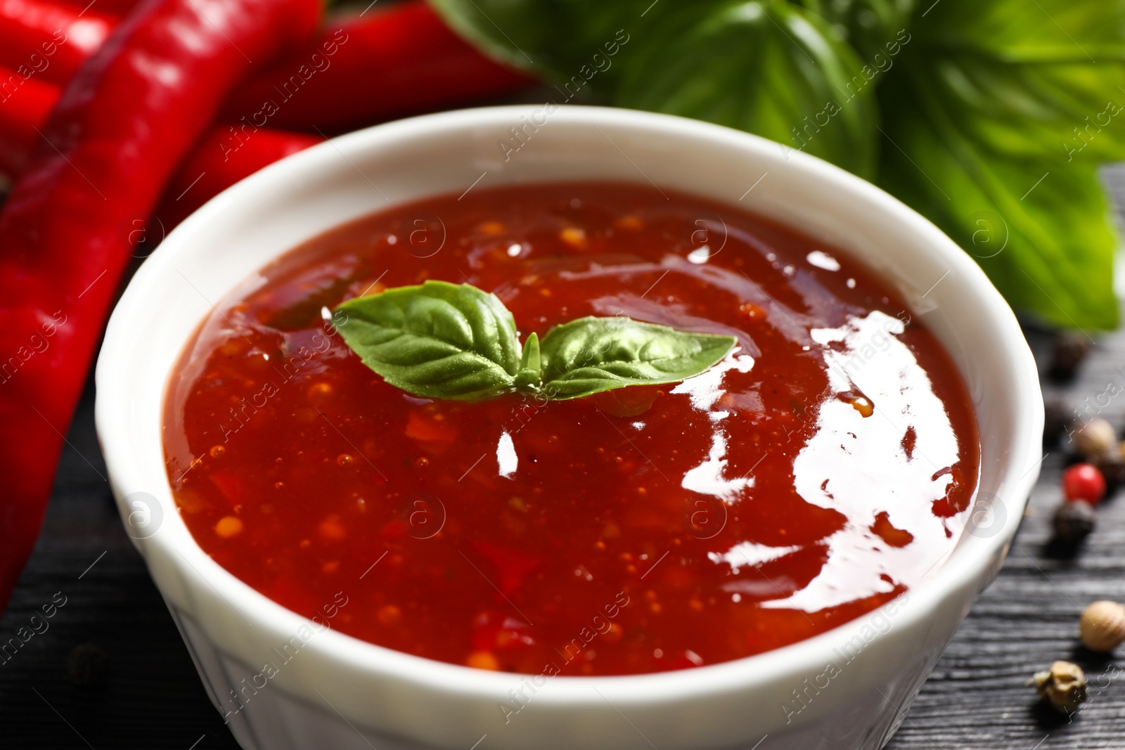 Photo of Spicy chili sauce with basil on dark table, closeup