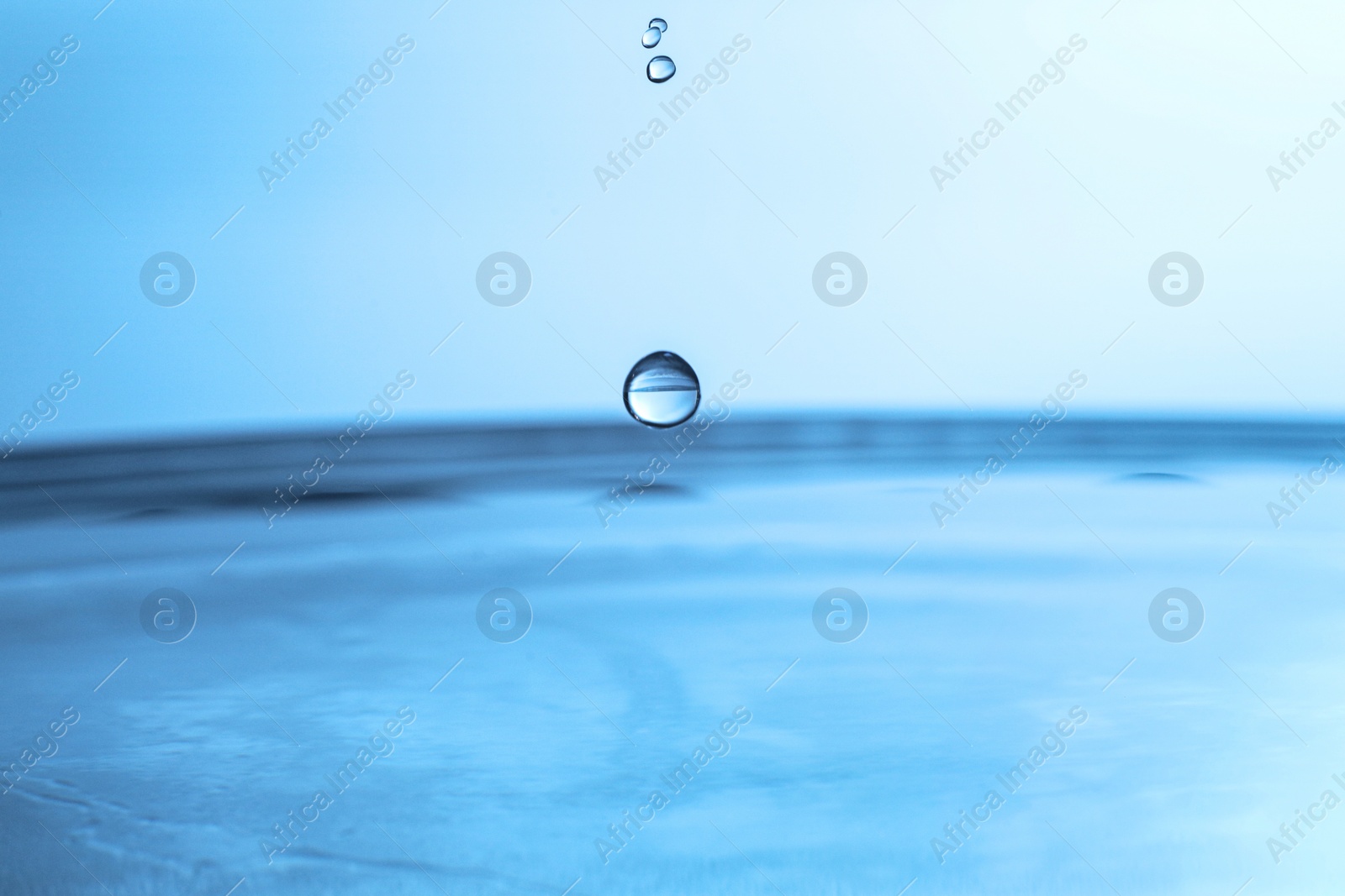 Photo of Drops falling into clear water on blue background, closeup