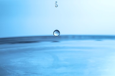 Photo of Drops falling into clear water on blue background, closeup