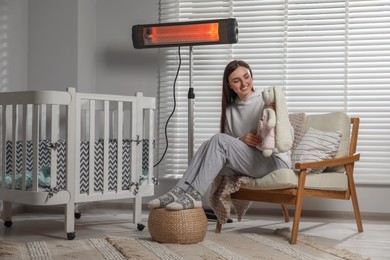 Photo of Young woman with knitted rabbit and modern electric infrared heater in child room