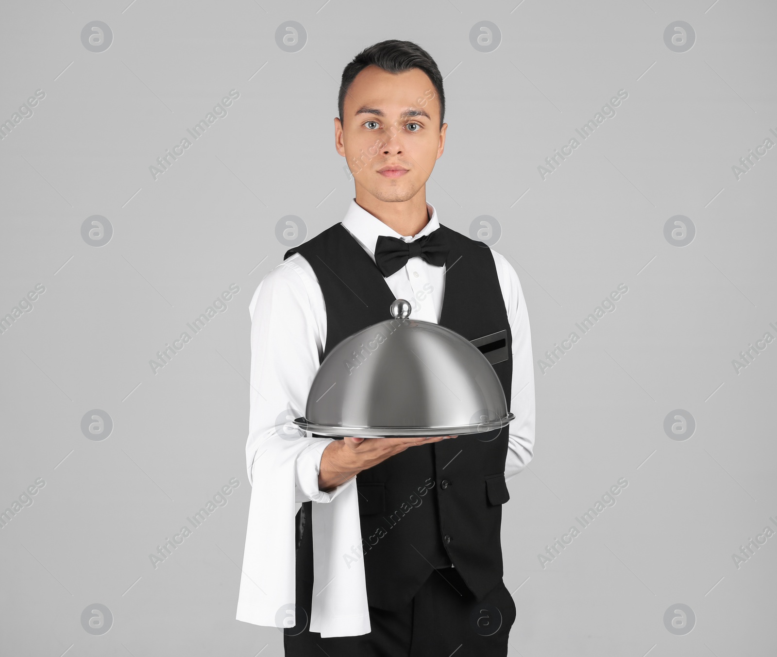 Photo of Waiter holding metal tray with lid on grey background