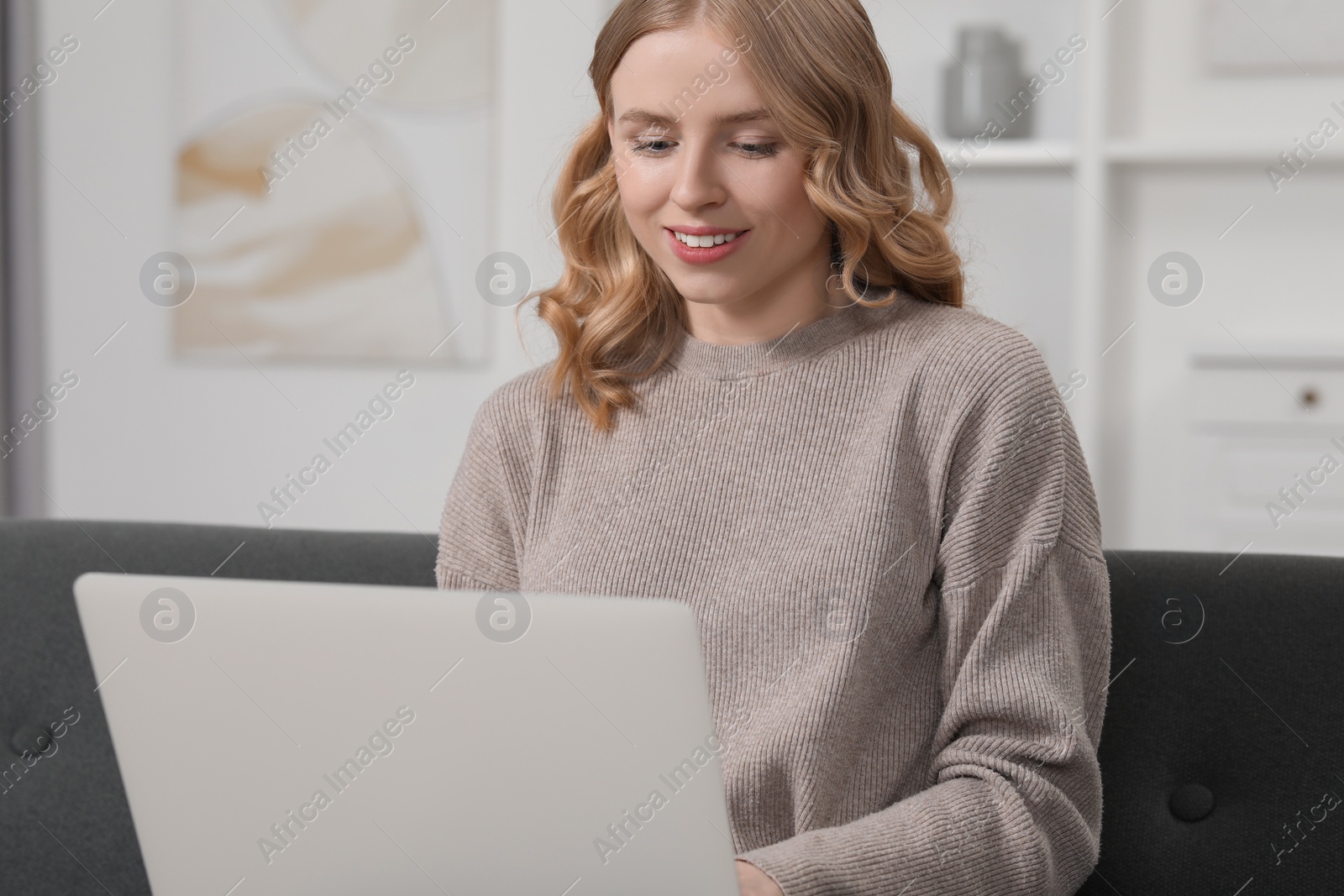 Photo of Beautiful woman with blonde hair using laptop on sofa at home