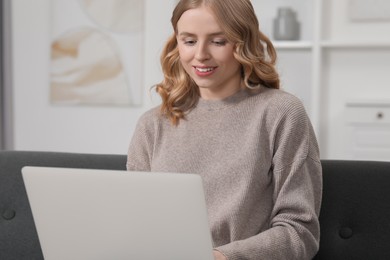 Beautiful woman with blonde hair using laptop on sofa at home