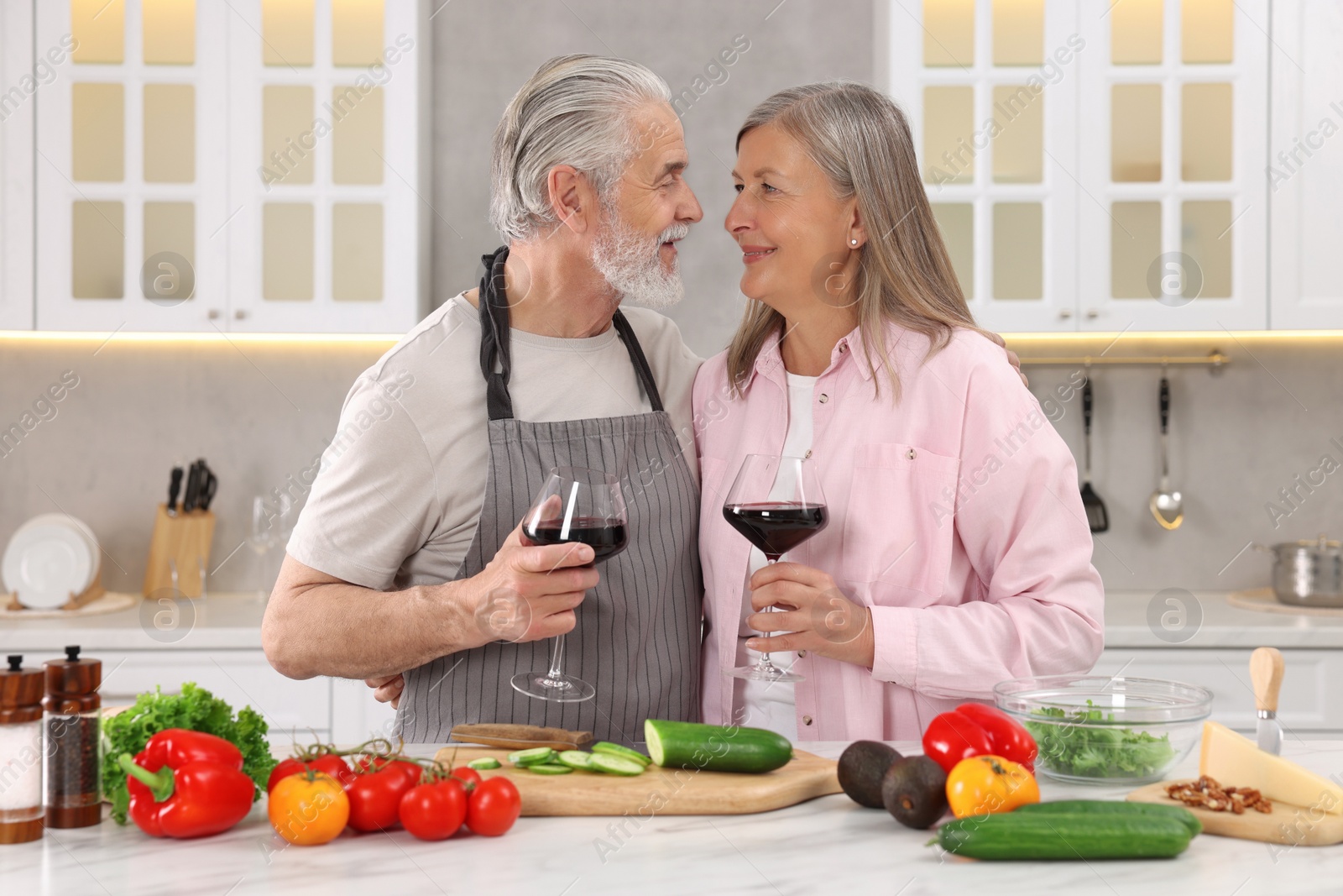 Photo of Happy affectionate senior couple with glasses of wine in kitchen