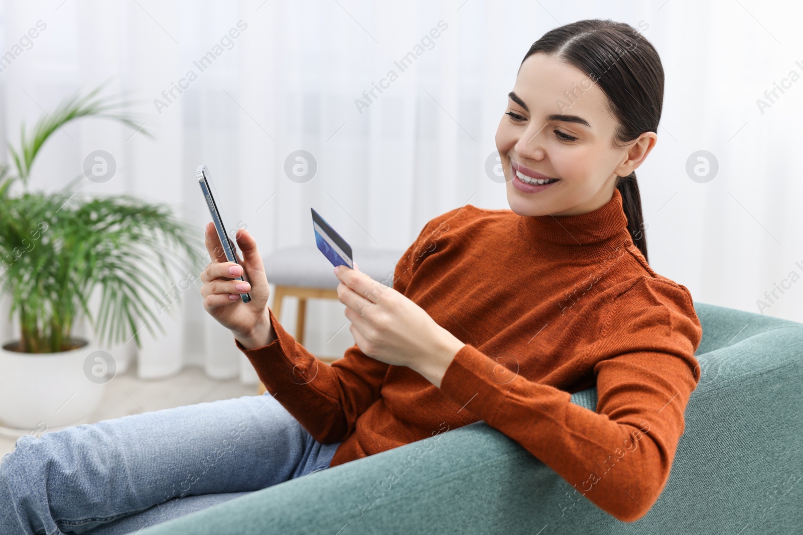 Photo of Happy young woman with smartphone and credit card shopping online on sofa at home