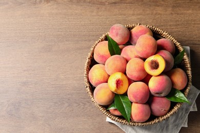 Photo of Cut and whole fresh ripe peaches with green leaves in basket on wooden table, top view. Space for text