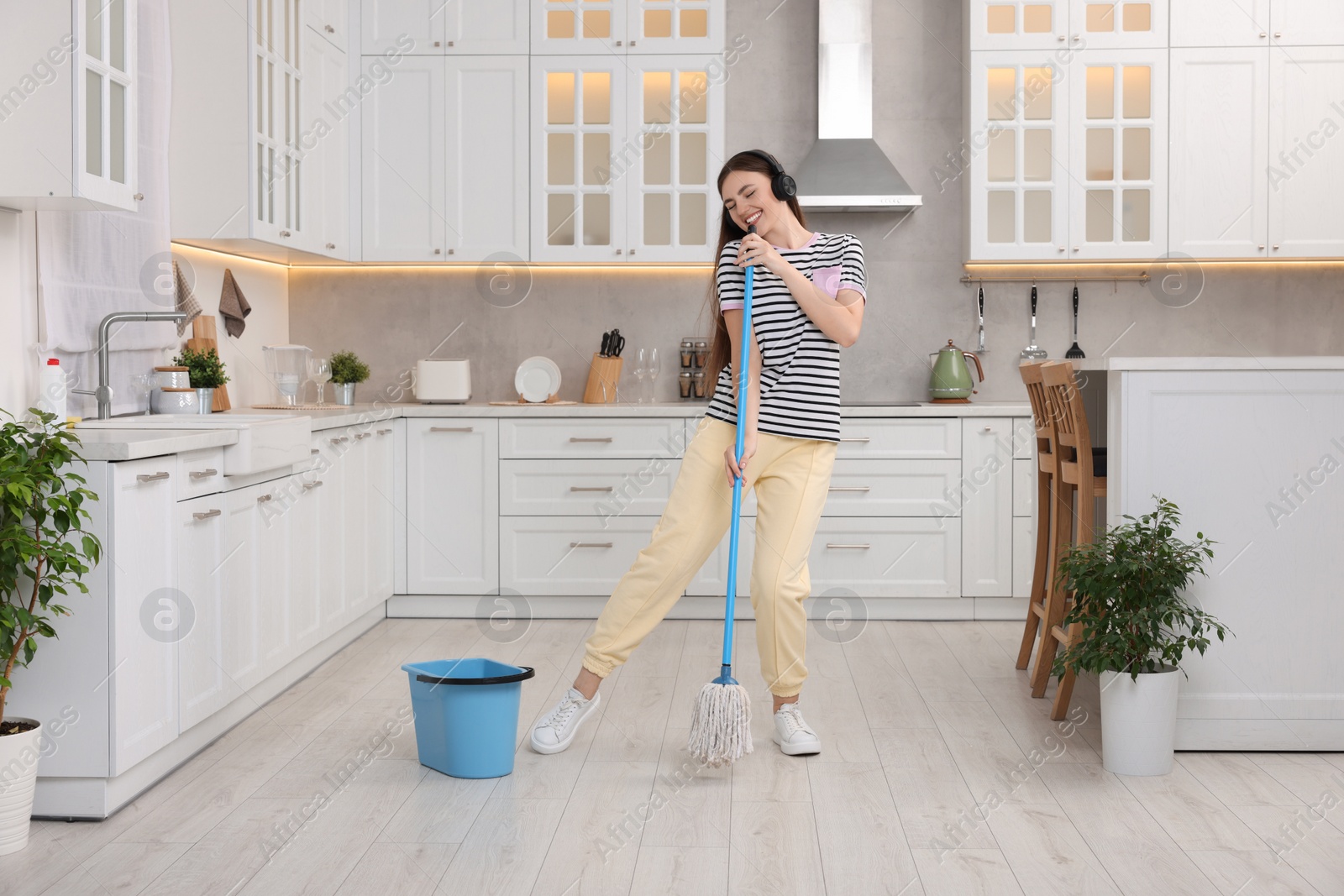 Photo of Enjoying cleaning. Happy woman with mop singing while tidying up in kitchen