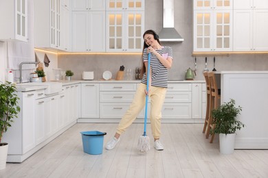 Photo of Enjoying cleaning. Happy woman with mop singing while tidying up in kitchen