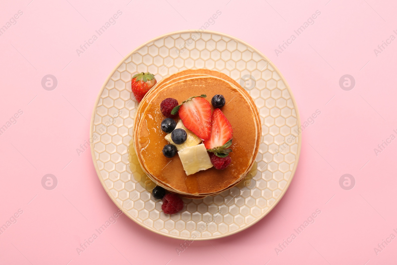 Photo of Delicious pancakes with fresh berries, butter and honey on pink background, top view