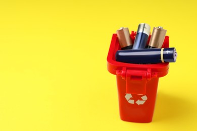 Used batteries in recycling bin on yellow background, space for text