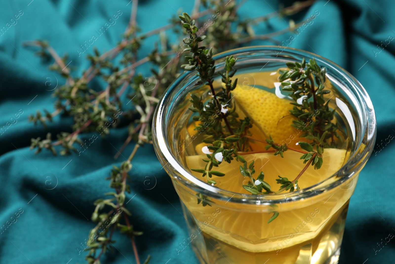 Photo of Glass of aromatic herbal tea with thyme and lemon on teal fabric, closeup. Space for text