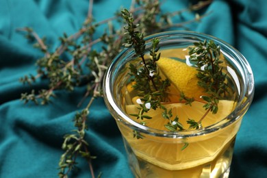 Photo of Glass of aromatic herbal tea with thyme and lemon on teal fabric, closeup. Space for text