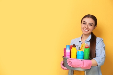 Woman with basin of detergents on color background. Space for text