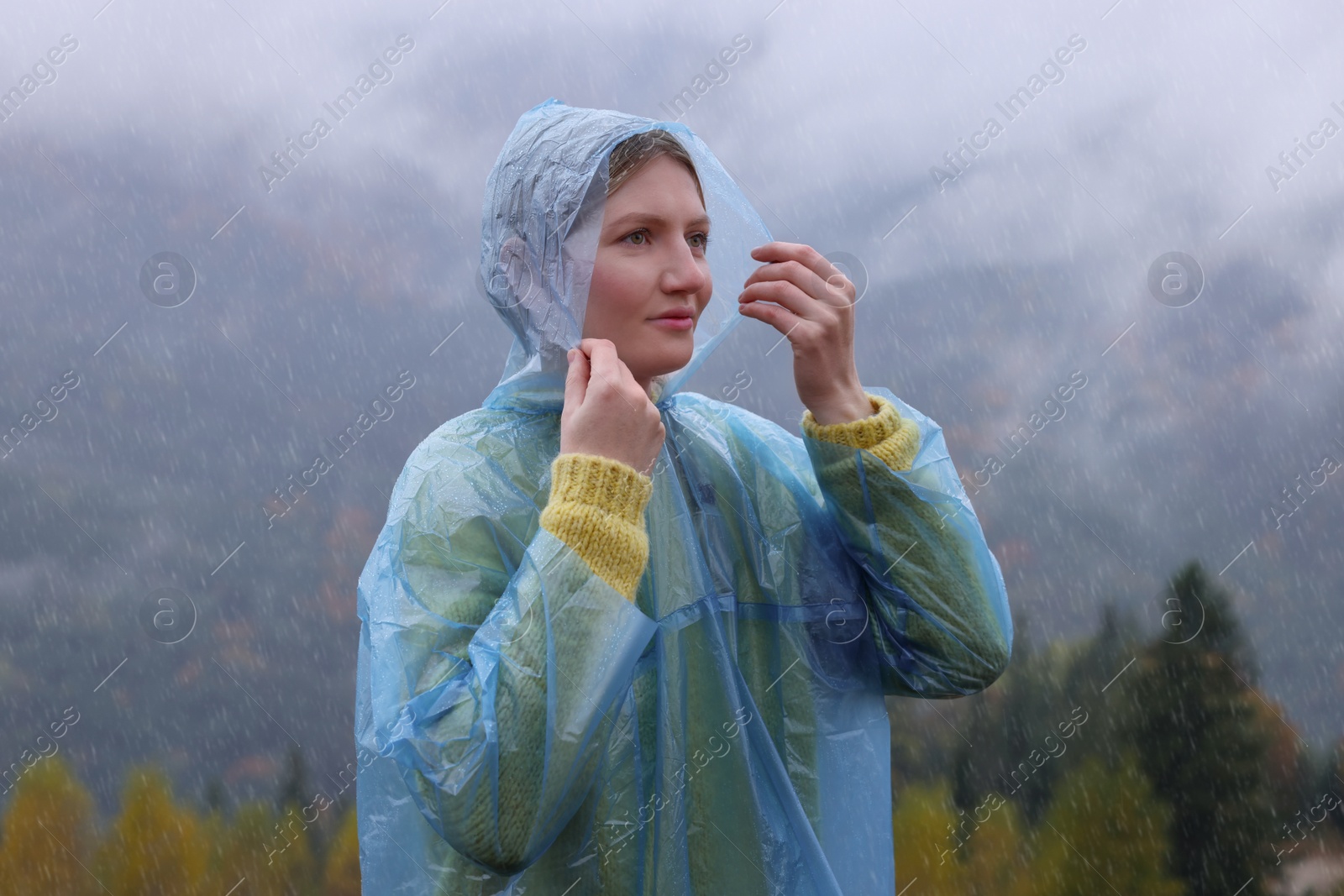 Photo of Young woman in raincoat enjoying mountain landscape under rain