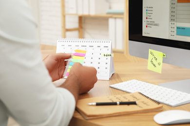 Man putting sticker on calendar at table in office, closeup