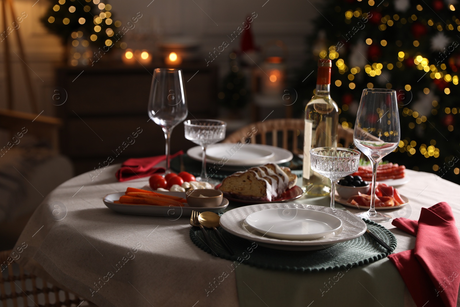 Photo of Christmas table setting with bottle of wine, appetizers and dishware indoors