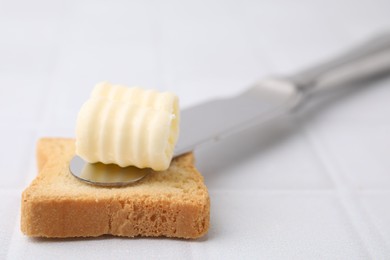 Photo of Tasty butter curl, knife and piece of dry bread on white tiled table, closeup