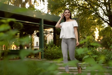 Photo of Beautiful young woman walking in green park, space for text