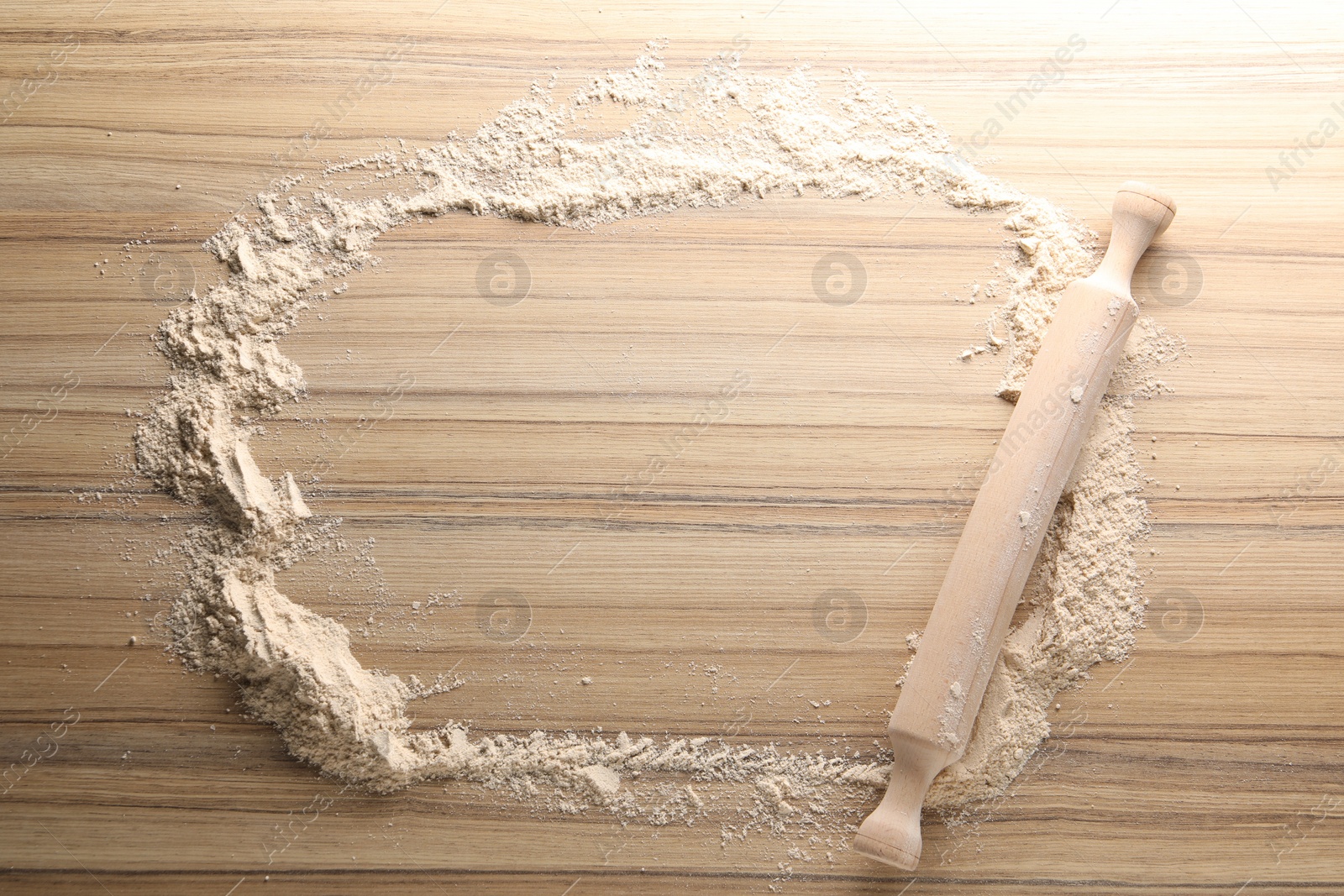 Photo of Scattered flour and rolling pin on wooden table, top view. Space for text