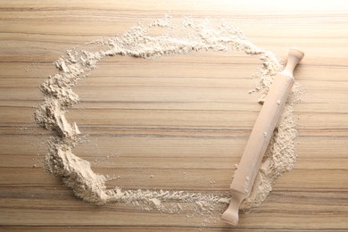 Scattered flour and rolling pin on wooden table, top view. Space for text