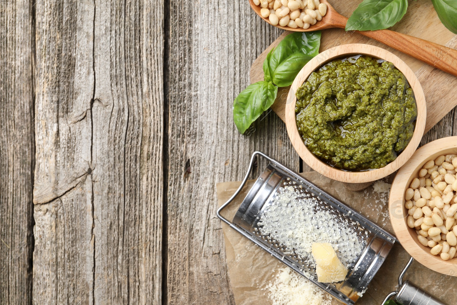 Photo of Tasty pesto sauce, basil, pine nuts and cheese on wooden table, top view. Space for text