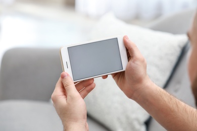 Young man using video chat on smartphone in living room, closeup. Space for design