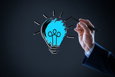 Image of Idea concept. Businessman drawing glowing light bulb illustration on virtual screen, closeup