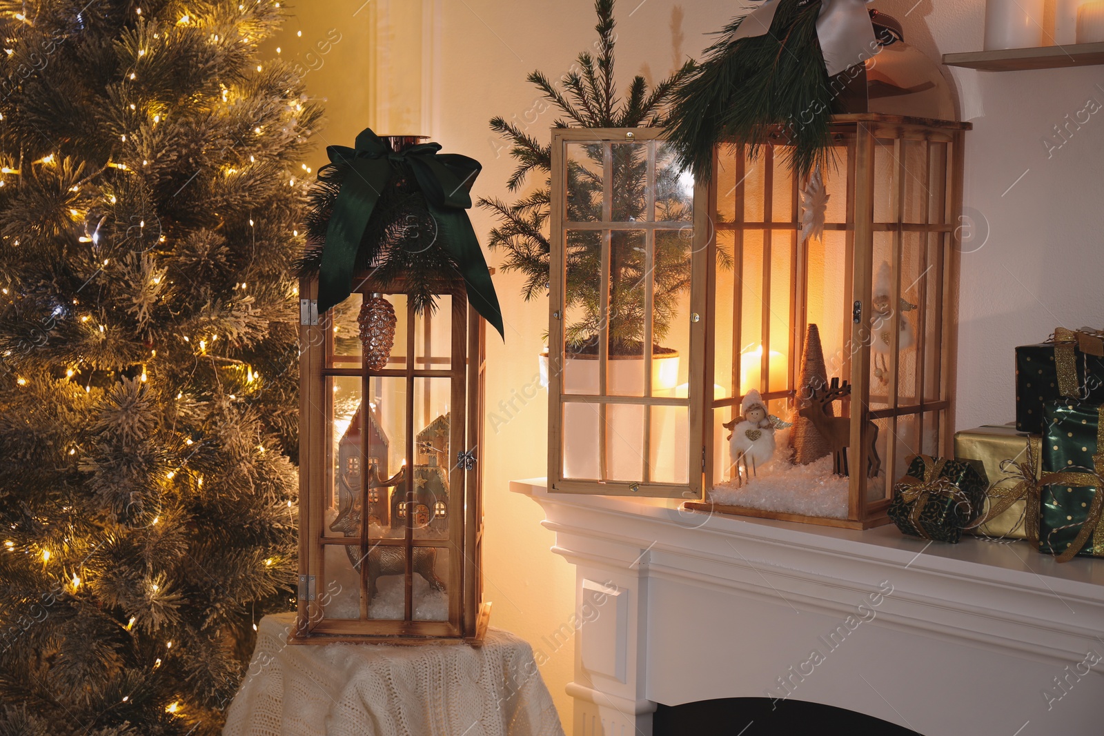 Photo of Beautiful wooden lanterns and other decorations on mantelpiece in room with Christmas tree