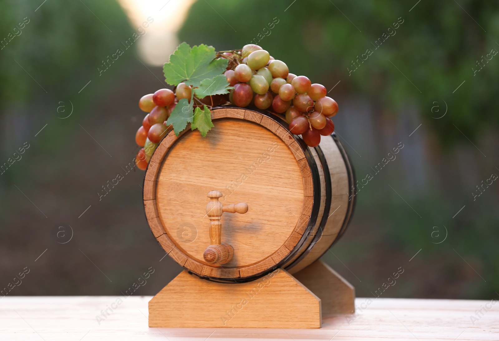 Photo of Wooden wine barrel with ripe grapes on table outdoors
