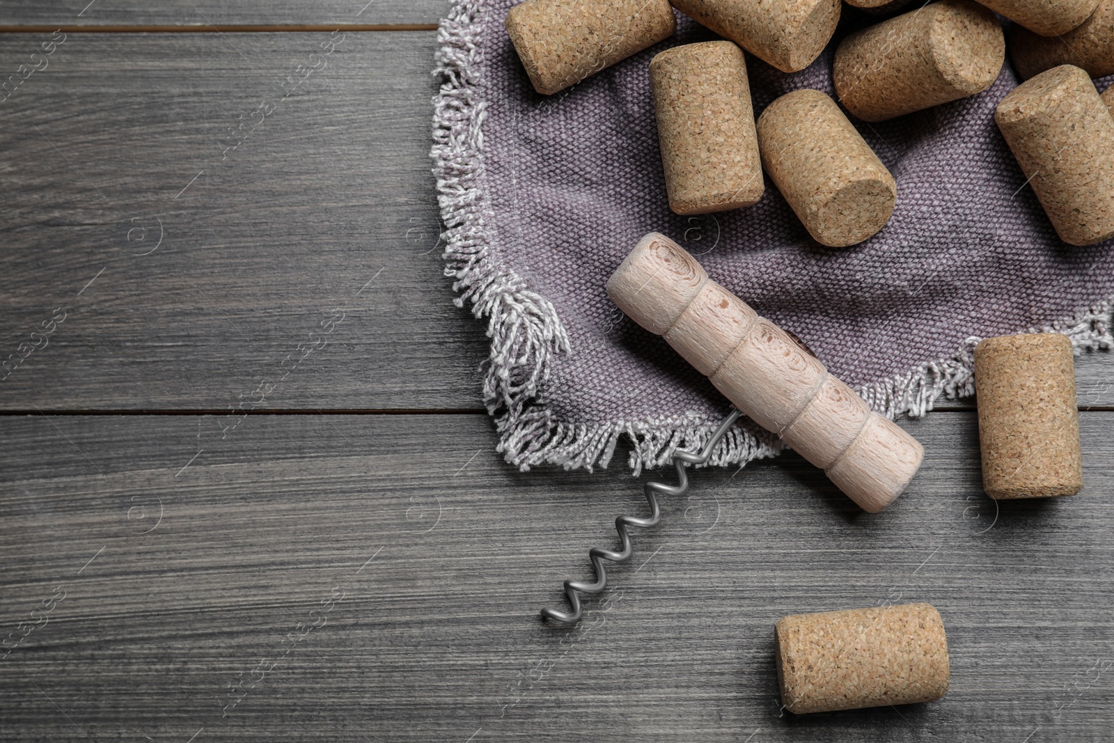 Photo of Corkscrew and wine bottle stoppers with napkin on wooden table, flat lay. Space for text