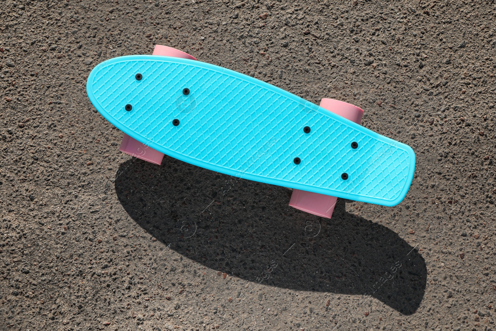 Photo of Modern light blue skateboard with pink wheels on asphalt road outdoors, top view