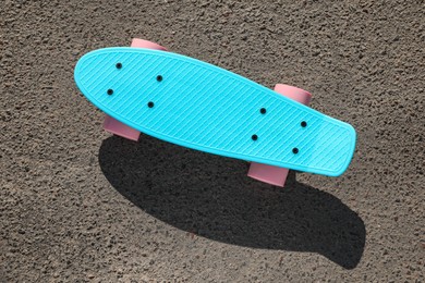 Modern light blue skateboard with pink wheels on asphalt road outdoors, top view