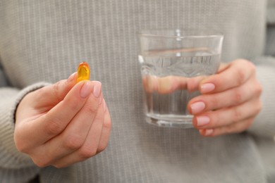 Woman holding glass of water and pill, closeup view